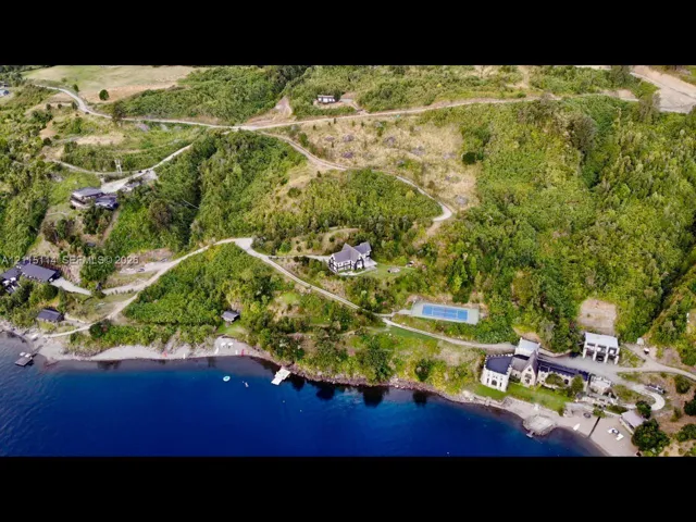 Aerial perspective of waterfront estate featuring extensive shoreline, private tennis court, winding paved access roads, and hillside landscape