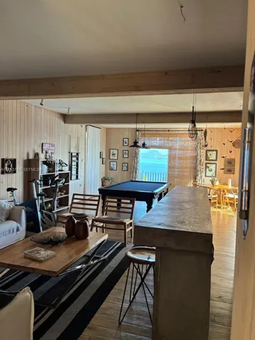 Interior featuring light-toned wood-paneled walls, exposed wood ceiling beams, a built-in stone-top bar, wood-finish flooring, and a window framing a water horizon