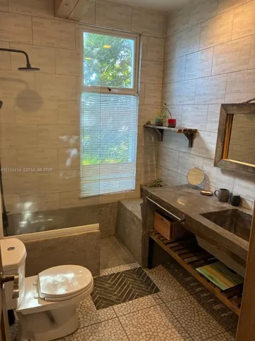Concrete vanity with integrated basin, textured wall tiling, open slatted shelving, glass-enclosed shower, and pebbled floor tile