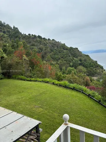 Manicured lawn bordered by a low-profile landscape fence, mature hillside forest, and coastal water backdrop