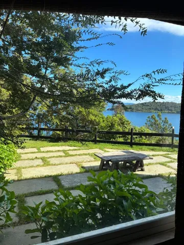 Stone-paver patio with integrated turf seams, horizontal rail fencing, and mature trees overlooking a waterfront landscape