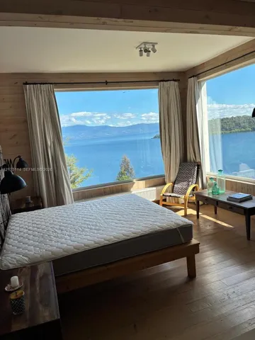 Interior space featuring natural wood wall paneling, wood-finish flooring, and expansive panoramic windows framing a mountain and water backdrop