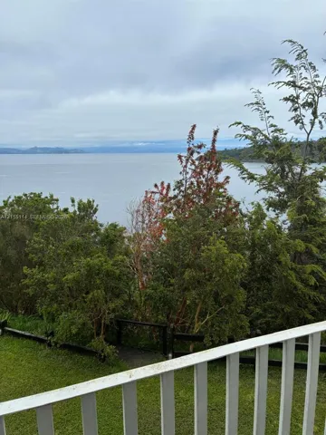 Elevated outdoor space featuring white picket railing, manicured lawn, wooden steps, and expansive water scenery