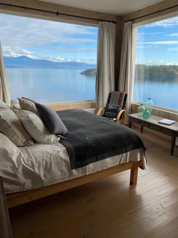 Floor-to-ceiling windows, wood-finish flooring, natural wood paneled walls, and expansive water and mountain scenery