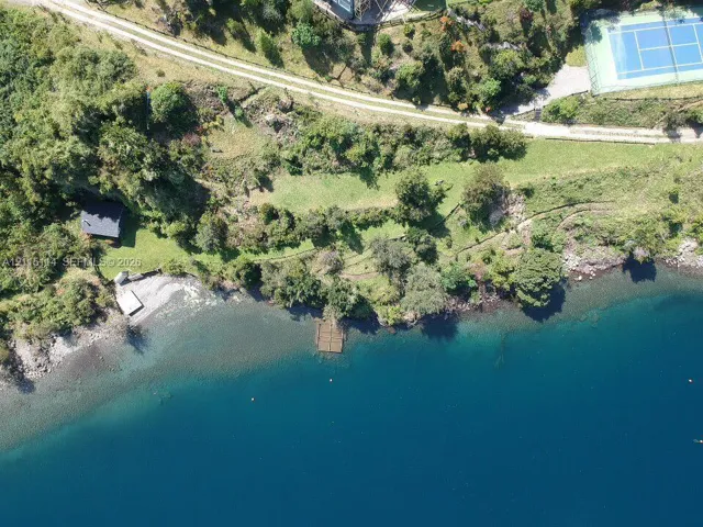 Aerial perspective of waterfront parcel featuring a private dock, rocky shoreline, tennis court, and expansive natural landscape