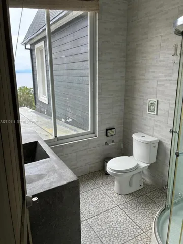 Bathroom featuring textured tile wall cladding, custom concrete sink, pebble-stone flooring, and a glass-enclosure shower