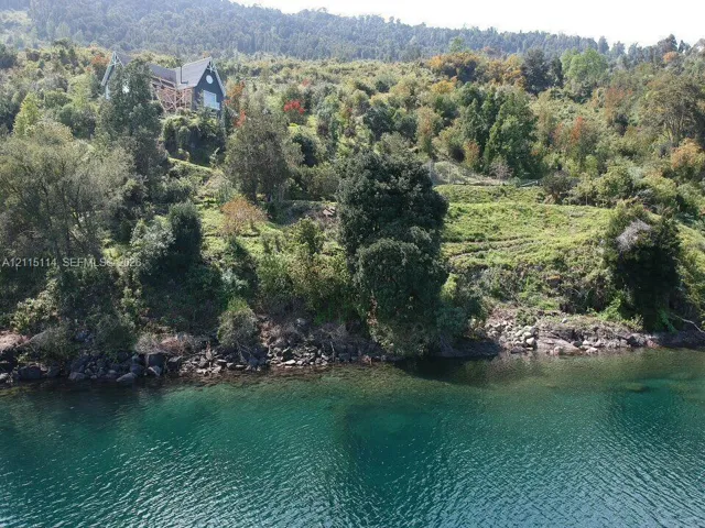 Waterfront property featuring sloped topography, mature trees, rock shoreline, and tiered landscaping