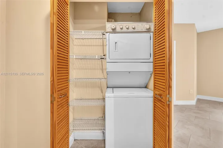 Laundry closet featuring louvered wooden doors, a stacked washer and dryer unit, and built-in wire shelving