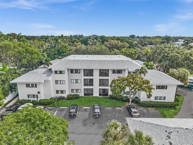 Three-story multi-unit structure featuring a light-toned stucco exterior, a hip roof with asphalt shingles, private balconies, and dedicated surface parking