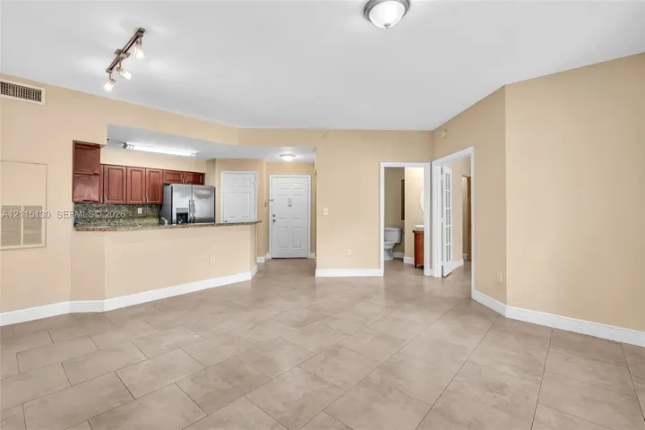 Open-concept interior featuring large-format tile flooring, kitchen with granite countertops and wood cabinetry, stainless steel refrigerator, and recessed track lighting
