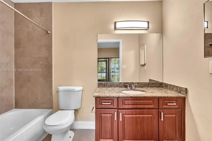 Bathroom featuring a vanity with wood-finish cabinetry, stone countertop, integrated sink, and wall-mounted light fixture, paired with a shower and tub combination featuring ceramic wall tile