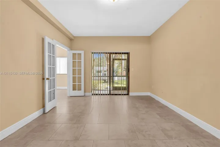 Interior space featuring neutral wall paint, large-format tile flooring, white-framed French doors, and sliding glass doors with vertical blinds