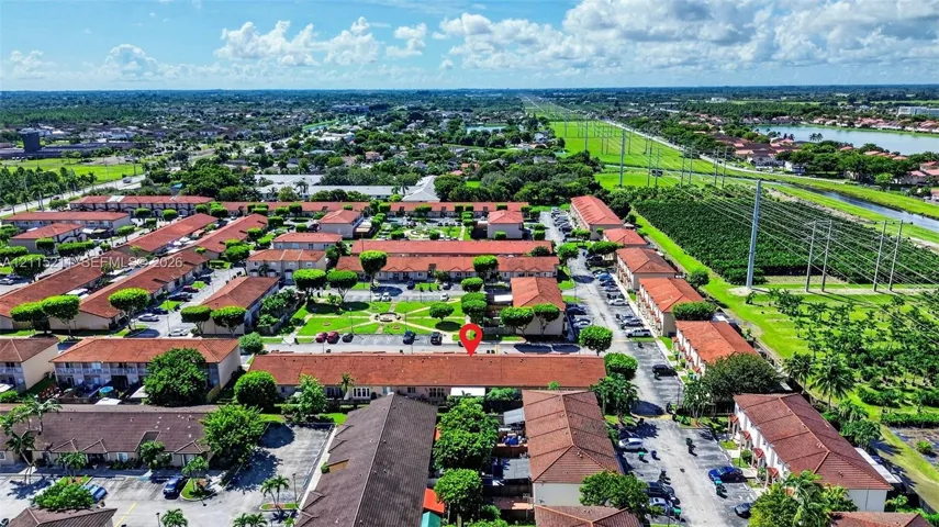 Aerial perspective of a multi-unit complex featuring tiled roofs, paved parking surfaces, and landscaped grounds with established greenery