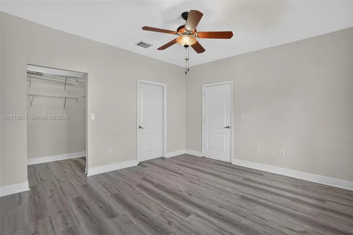 Neutral-toned interior featuring wood-finish flooring, a multi-blade ceiling fan with integrated lighting, two-panel interior doors, and a built-in closet with wire shelving