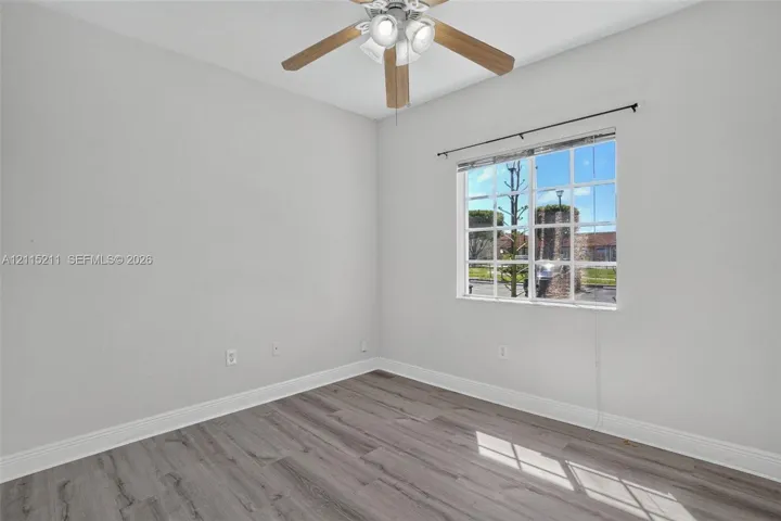 Room featuring wood-finish flooring, a multi-pane window with a curtain rod, and a ceiling fan with integrated lighting