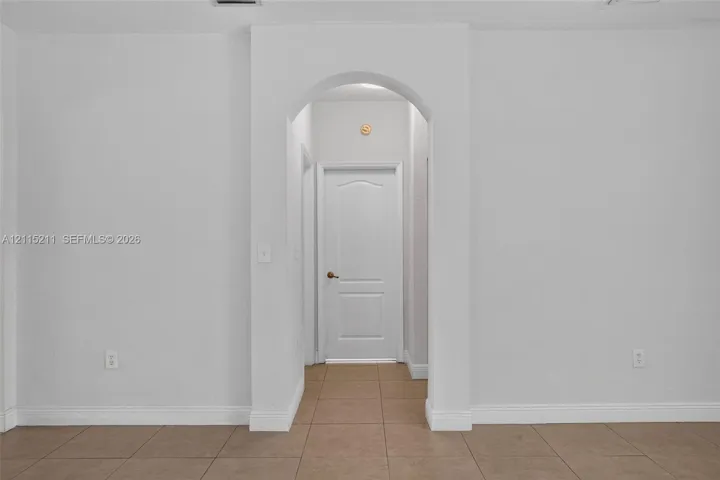 Arched doorway featuring a six-panel interior door and neutral tile flooring