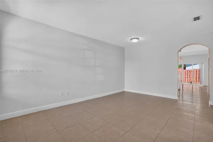 Neutral-toned interior space featuring large-format ceramic floor tiles, a structural arched doorway, and a ceiling-mounted light fixture
