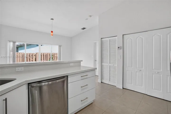 Kitchen featuring a peninsula with solid-surface countertops, stainless steel dishwasher, tile flooring, vaulted ceilings, and louvered-style closet doors