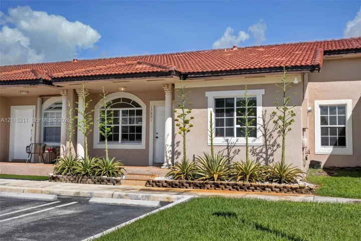 Stucco exterior featuring a red tile roof, decorative columns, arched window detailing, and raised stone garden beds