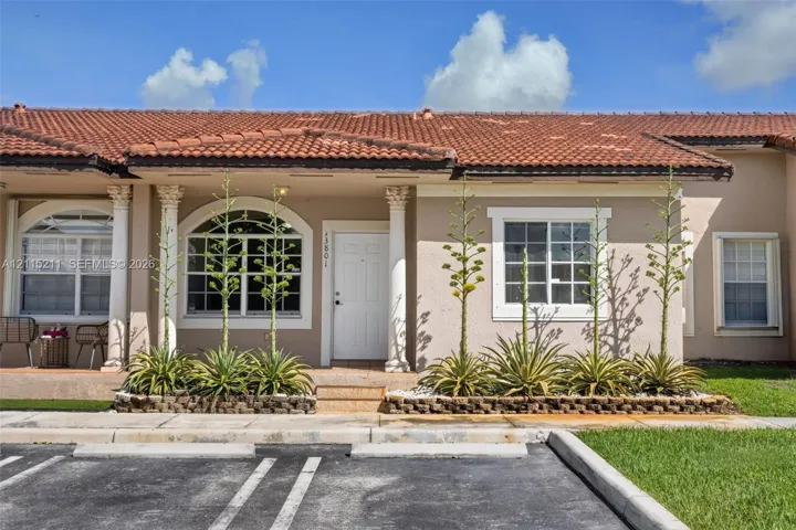 Single-story stucco exterior featuring a clay tile roof, arched windows, decorative columns, and landscaped masonry planters