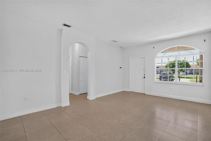 Neutral-toned ceramic tile flooring, arched entryway, and large windows featuring an arched top pane