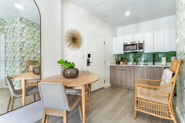 Kitchen area featuring two-tone cabinetry, stainless steel microwave, green glass tile backsplash, wood-finish flooring, and arched floor mirror