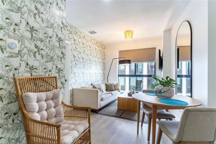 Patterned botanical wallpaper, wood-finish flooring, floor-to-ceiling windows with roller shades, a flush-mount geometric ceiling light fixture, and an arched wall-mounted mirror