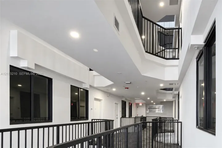 Multi-level walkway featuring black metal railings, recessed ceiling lighting, and large windows with black frames
