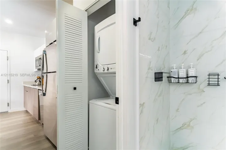 Stacked laundry unit concealed behind louvered doors, stone-finish wall tile, and built-in matte black wall-mounted shelving