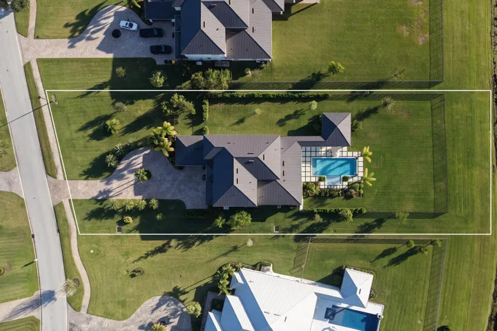 Aerial perspective of a sprawling property featuring a multi-gabled roofline, a paved circular driveway, a rectangular inground pool, and a fully fenced perimeter