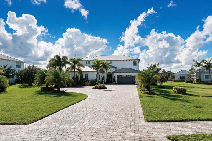 Two-story exterior featuring white stucco siding, a metal roof, an attached garage, and a paver driveway set within a landscaped lawn