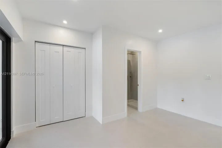 Interior space featuring large-format neutral floor tile, recessed ceiling lighting, a bi-fold closet, and a doorway revealing a tiled shower enclosure