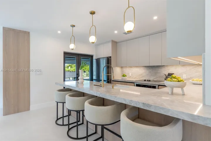 Kitchen featuring a waterfall-edge stone countertop, custom flat-panel cabinetry, gold-finish pendant lighting, and an integrated appliance package