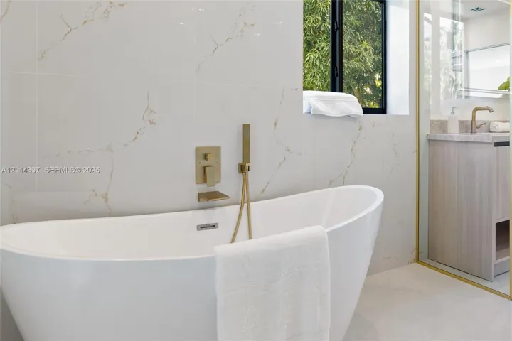 Freestanding soaking tub featuring wall-mounted metallic fixtures and a handheld shower spray, set against large-format tile walls with prominent veining