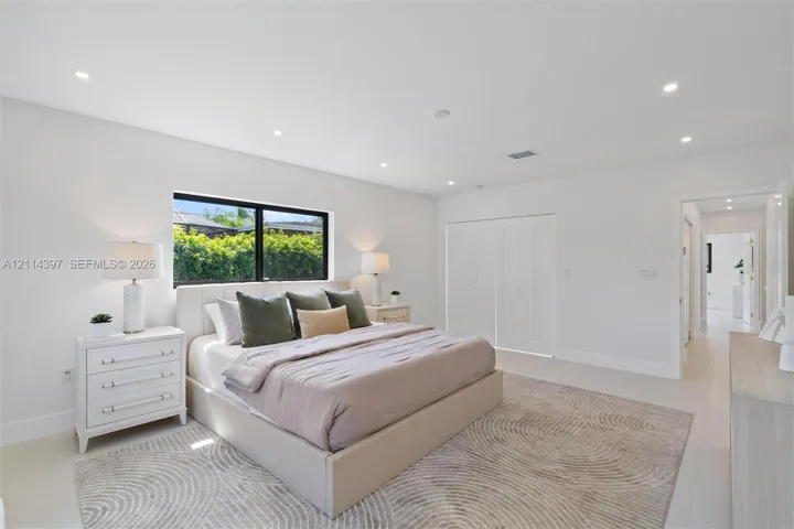 Neutral-toned room featuring recessed lighting, a large window with black framing, and multi-panel interior closet doors