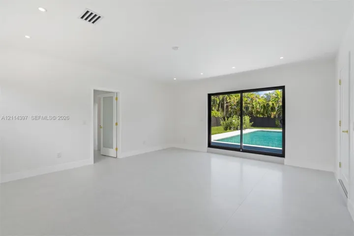 Open interior space featuring light-toned tile flooring, recessed ceiling lighting, a sliding glass door with a dark frame, and a frosted glass panel door