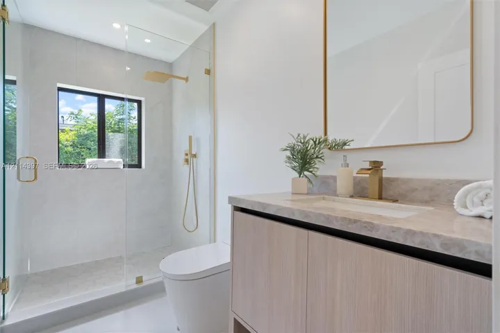 Modern vanity with stone-finish countertop, undermount sink, brass-tone hardware, wall-mounted mirror, and glass-enclosed walk-in shower with rainfall showerhead
