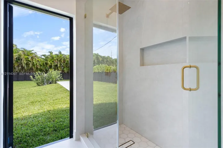 Walk-in shower featuring large-format stone-tile walls, hexagonal floor tiling, a recessed wall niche, a brass-finish rainfall showerhead, and a floor-to-ceiling glass panel with a matching brass-finish handle