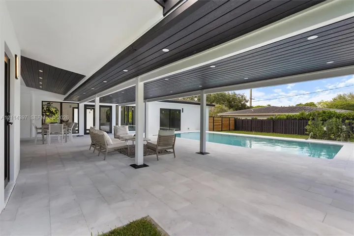Covered outdoor patio featuring large-format tile flooring, recessed ceiling lighting, and a wood-finish ceiling, overlooking a rectangular swimming pool with integrated hardscaping