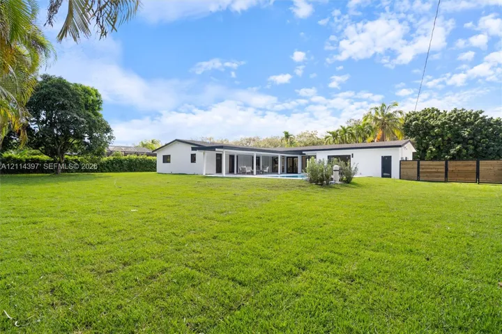 Expansive backyard featuring a sprawling lawn, mature trees, a horizontal-plank wood privacy fence, and a covered patio