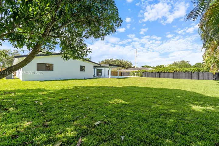 Expansive backyard featuring a large grass lawn, perimeter privacy fencing, mature trees, and a covered rear patio