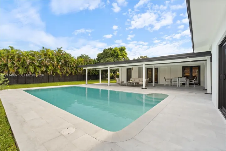 Rectangular swimming pool featuring integrated steps, expansive stone-paver decking, and a covered lanai with recessed lighting