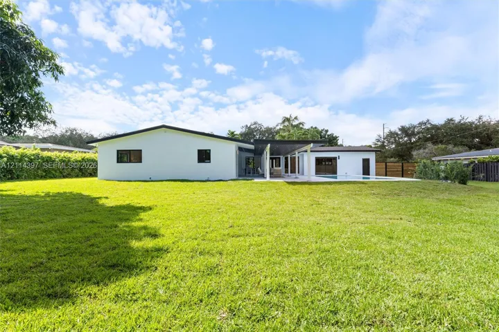 Expansive backyard featuring a sprawling lawn, swimming pool, covered patio, and perimeter privacy fencing