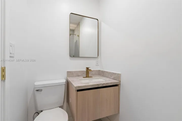 Floating vanity with a stone-finish countertop, undermount rectangular sink, brass-finish faucet, and rectangular wall-mounted mirror