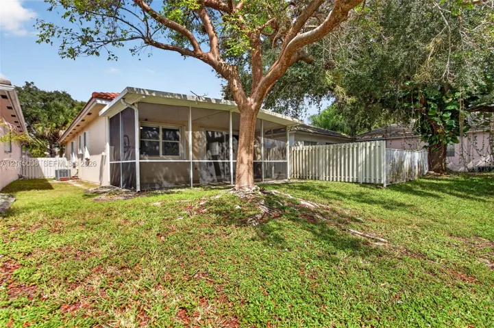 Screened-in rear porch featuring a red tile roof, mature landscaping, and white privacy fencing