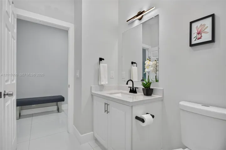 Bathroom featuring a white vanity with a composite stone countertop, rectangular undermount sink, matte black faucet, and linear LED wall-mounted light fixture
