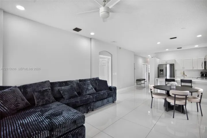 Large-format tile flooring, recessed ceiling lighting, ceiling fan, and white kitchen cabinetry with stainless steel appliances
