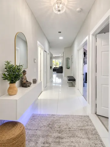 Hallway featuring large-format tile flooring, a wall-mounted floating console, an arched wall mirror, and a decorative flush-mount ceiling fixture