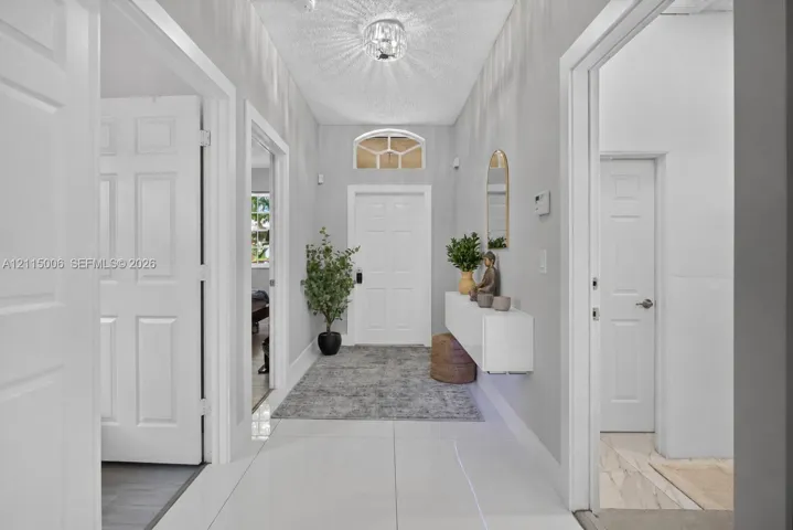 Entryway featuring large-format tile flooring, a six-panel entry door with an arched transom window, a wall-mounted floating console, and a central crystal-style flush-mount light fixture