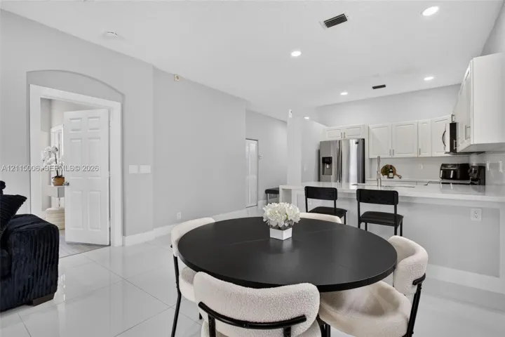 Kitchen featuring white cabinetry, solid-surface countertops, a stainless steel refrigerator, and recessed lighting, accented by light-toned tile flooring and an arched entryway